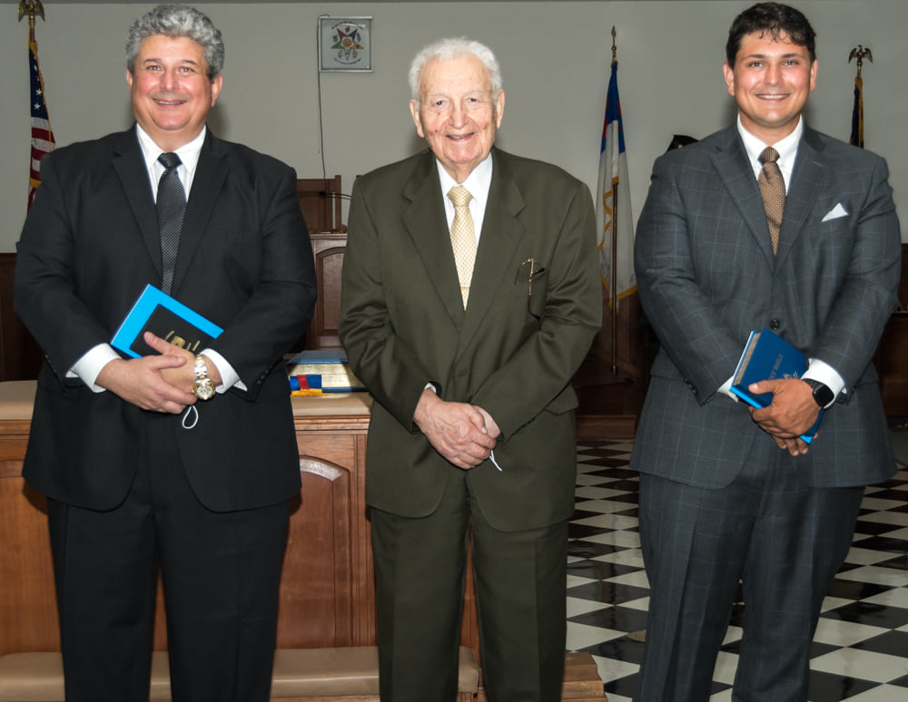 Three generations of Master Masons standing together — a grandfather at center, with his son and grandson on either side